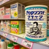 A popular and scarce can of powdered milk on a store shelf, with other baby products in the background, photographed in a Japanese store.