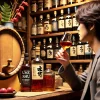 A popular setting showcasing umeshu (plum wine) aged in a whisky barrel, with a Japanese person enjoying a glass of the drink in a cozy bar. The background features a shelf filled with various bottles of umeshu and whisky, emphasizing its popularity.