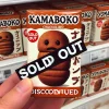 3. A small chocolate snack shaped like a 'kamaboko' with a baked, firm outer layer. A large 'sold out' or 'discontinued' sign is placed next to the snack in a store shelf, emphasizing the confusion of it being discontinued.