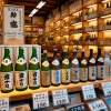 A store shelf in Japan displaying bottles of a rare Japanese sake from a small Toyama brewery. The shelf is neatly arranged with sake bottles, and the store has a traditional yet modern atmosphere. Signs in Japanese indicate limited availability of this exclusive sake.