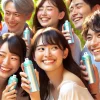 A group of Japanese people feeling refreshed and happy after using an unscented deodorant spray. They are smiling and interacting in a bright, outdoor environment, enjoying the fresh feeling from the deodorant. The deodorant spray cans are visible in the scene.